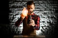 Young male bartender holds black ceramic glass with slice of citrus and make fire