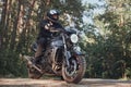 Young male biker in a helmet travels on a motorcycle alone, on a road in the forest