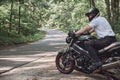 Young male biker in a helmet travels on a motorcycle alone, on a road in the forest