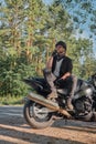 Young male biker in helmet travels on a motorcycle alone, stopped and smoking on the side of a forest road Royalty Free Stock Photo