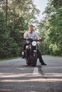 Young male biker travels on a motorcycle alone, on an asphalt road in the forest Royalty Free Stock Photo