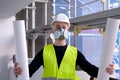 Young male builder engineer, worker or architect in white hardhat and protective respirator during inspection in construction site