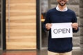 Young male business owner holding OPEN sign near cafe, closeup. Space for text Royalty Free Stock Photo