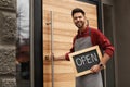 Young male business owner holding OPEN sign near cafe. Space for text Royalty Free Stock Photo