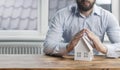 A young male businessman holds his hands over a miniature paper house. The concept of protection and security of property and home