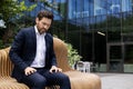 A young male businessman is sitting in a suit on the street outside an office center on a bench and is suffering from Royalty Free Stock Photo