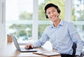 What can I help you with. a young male call center agent using a laptop and writing in a notebook at work. Royalty Free Stock Photo