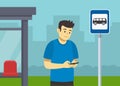 Young male character is using mobile phone while he waits for city bus. Close-up view of a passenger at bus stop. Royalty Free Stock Photo