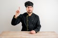 Young male chef in black uniform with her finger up has come up with an idea