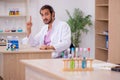 Young male chemist sitting at the desk in the classroom