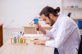 Young male chemist sitting at the desk in the classroom