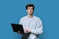 Young male college student using laptop, blue background