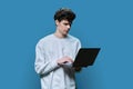 Young male college student using laptop, blue studio background