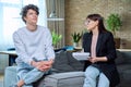 Young male communicates with female psychologist at therapy session in office Royalty Free Stock Photo