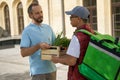 Young male courier with thermo bag giving wooden box with fresh