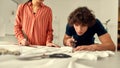 Born to create. Young male designer cutting white fabric textile in a studio. Group of creative millennials working Royalty Free Stock Photo