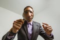 young male detective holding magnifying glass by right eye while standing in front of camera in isolation