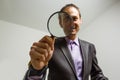 young male detective holding magnifying glass by right eye while standing in front of camera in isolation