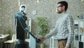 Young male developer and manlike robot cyborg shaking hands standing in office