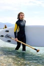 young male in diving suit spedting time at sea, carrying surfboard and paddle Royalty Free Stock Photo