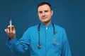 Young male doctor in a blue medical uniform looking in camera and holding a medical syringe for injection, isolated on Royalty Free Stock Photo