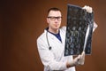 A young male doctor in glasses with a stethoscope around his neck holds an X-ray image of the spine in his hands Royalty Free Stock Photo