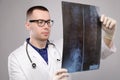 A young male doctor in glasses with a stethoscope around his neck holds an X-ray image of the spine in his hands Royalty Free Stock Photo