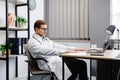 A young male doctor sits at his workplace and feels tired from work. A doctor takes a break from his work day because of pain