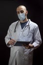 Young male doctor with stethoscope, wearing mask on face and holding a file while looking to the camera Royalty Free Stock Photo