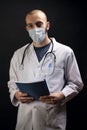 Young male doctor with stethoscope, wearing mask on face and holding a file while looking to the camera Royalty Free Stock Photo