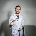 Young male dentist in a white coat holds a magnifying glass in front of his teeth and smiles. Concept humor in healthcare