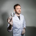 Young male dentist in a white coat holds a magnifying glass in front of his teeth and smiles. Concept humor in healthcare