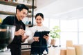 Young male and female barista cafe owner standing inside the coffee counter and talking about customer order from a tablet.