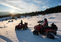 Young male and female riders on quad bikes on snow, enjoying sunset in the the mountains in winter Royalty Free Stock Photo