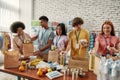 Young male and female volunteers packing food and drinks donation for homeless into boxes and paper bags, Small group of Royalty Free Stock Photo