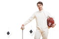 Young male fencer in fencing costume holding the sword and mask. target on background