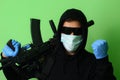 Criminal in a medical mask and sunglasses dressed in black clothes with a hood holds an automatic assault weapon Royalty Free Stock Photo