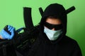 Young male gangster or criminal in a medical surgical mask and sunglasses holds an automatic assault weapon