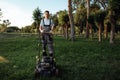 A young male gardener in overalls uses a lawn mower Royalty Free Stock Photo