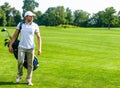 Young Male Golfer carries a Bag of Golf Clubs. Slim Man in White T-shirt , Golf Shoes, White Cap and Beige Pants is Royalty Free Stock Photo