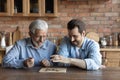 Young male grownup grandson play board game with elderly grandfather