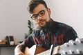 Young guitarist hipster at home with guitar playing thoughtful close-up