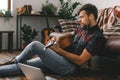 Young guitarist hipster at home sitting on the floor holding guitar listening earphones sound Royalty Free Stock Photo