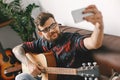 Young guitarist hipster at home holding guitar taking photos smiling Royalty Free Stock Photo