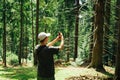 Young male hiker on a hike stands in the woods with a smartphone in his hand and takes a photo of a beautiful natural landscape in Royalty Free Stock Photo