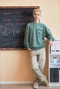 Young male hipster in grey pants and pullover standing by blackboard Royalty Free Stock Photo