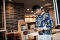 Young male indian freelancer in fast food cafe, handsome asian man reading text message during work on mobile phone in comfortable Royalty Free Stock Photo