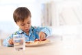 Young, male kid and eating breakfast at table for healthy, sandwich and hungry in house. Morning, food and water for