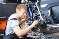 Young male locksmith disassembles motorcycle engine on bench in garage
