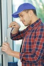 Young male locksmith installing lock on white door